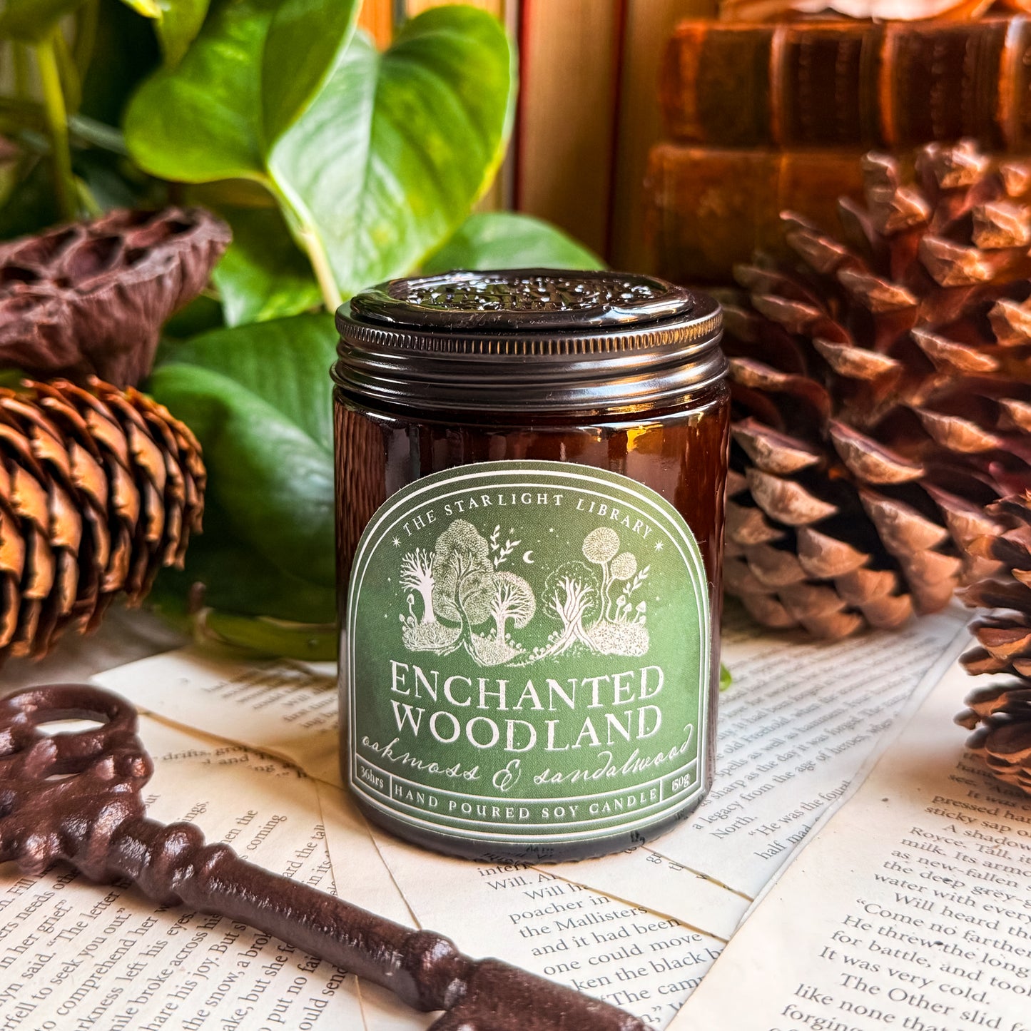 An Enchanted Woodlan Candle, surrounded by book pages, leaves and pinecones.