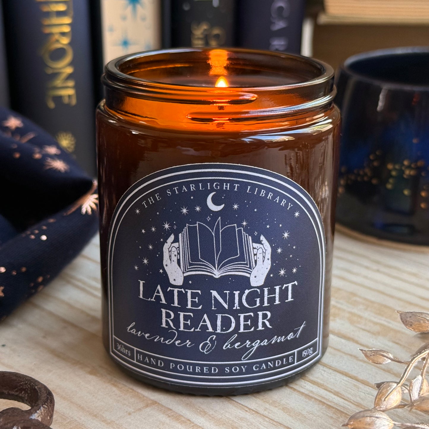 A Late Night Reader candle lit, surrounded by books and starry accessories.