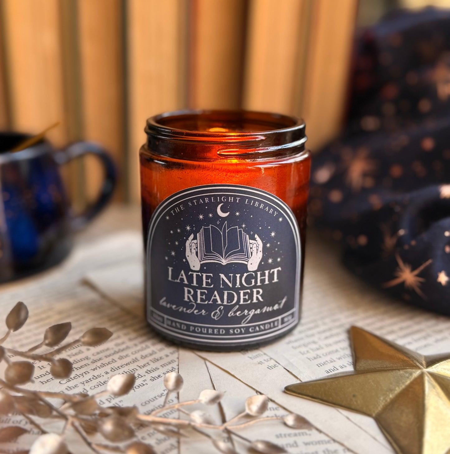 A Late Night Reader candle lit, surrounded by books and pages and starry accessories.