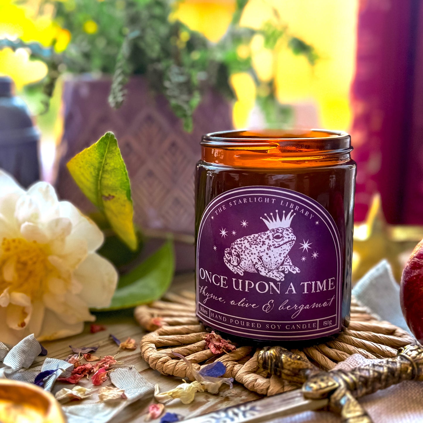 A Once Upon A Time Literary Candle. The candle is lit and surrounded by florals and fairytale iconography.