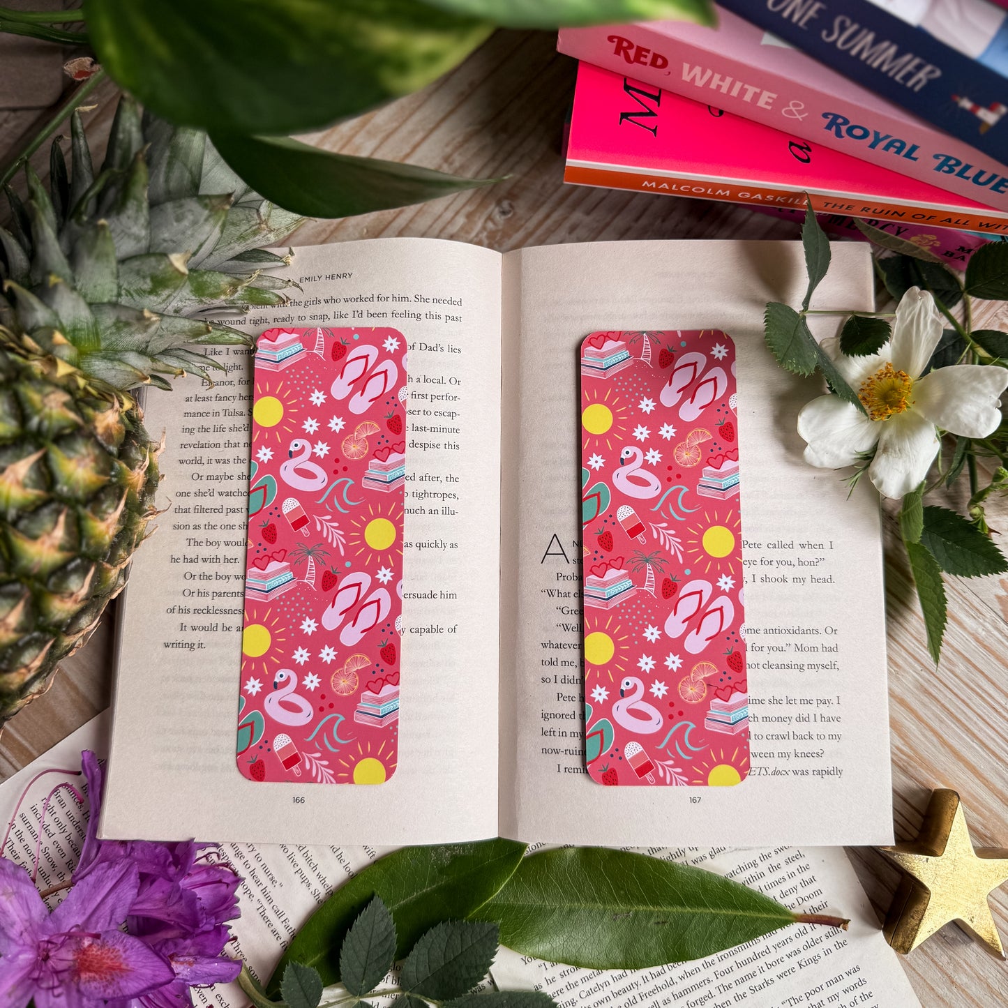 Two Paperback Paradise bookmarks, against a background of an open book, topical fruits and flowers.