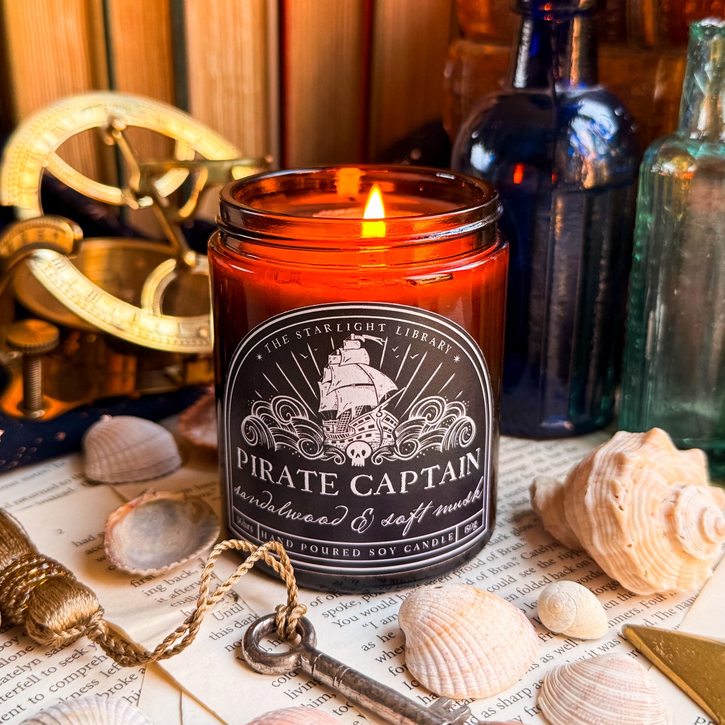 A Pirate Captain candle, lit, surrounded by shells, pages and glass bottles.