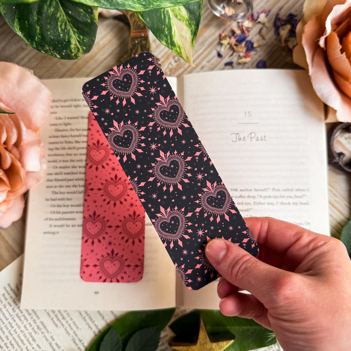 A hand holding the dark side of the romance reader bookmark above an open book.