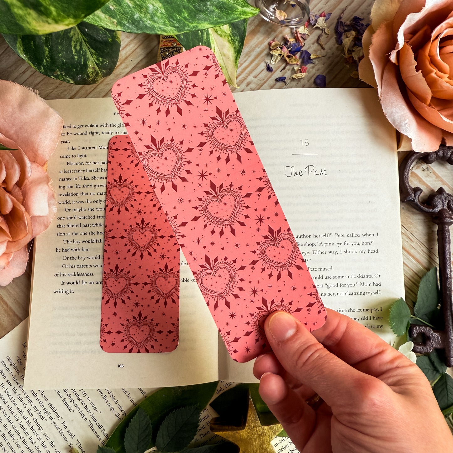 A hand holding the pink side of the romance reader bookmark above an open book.
