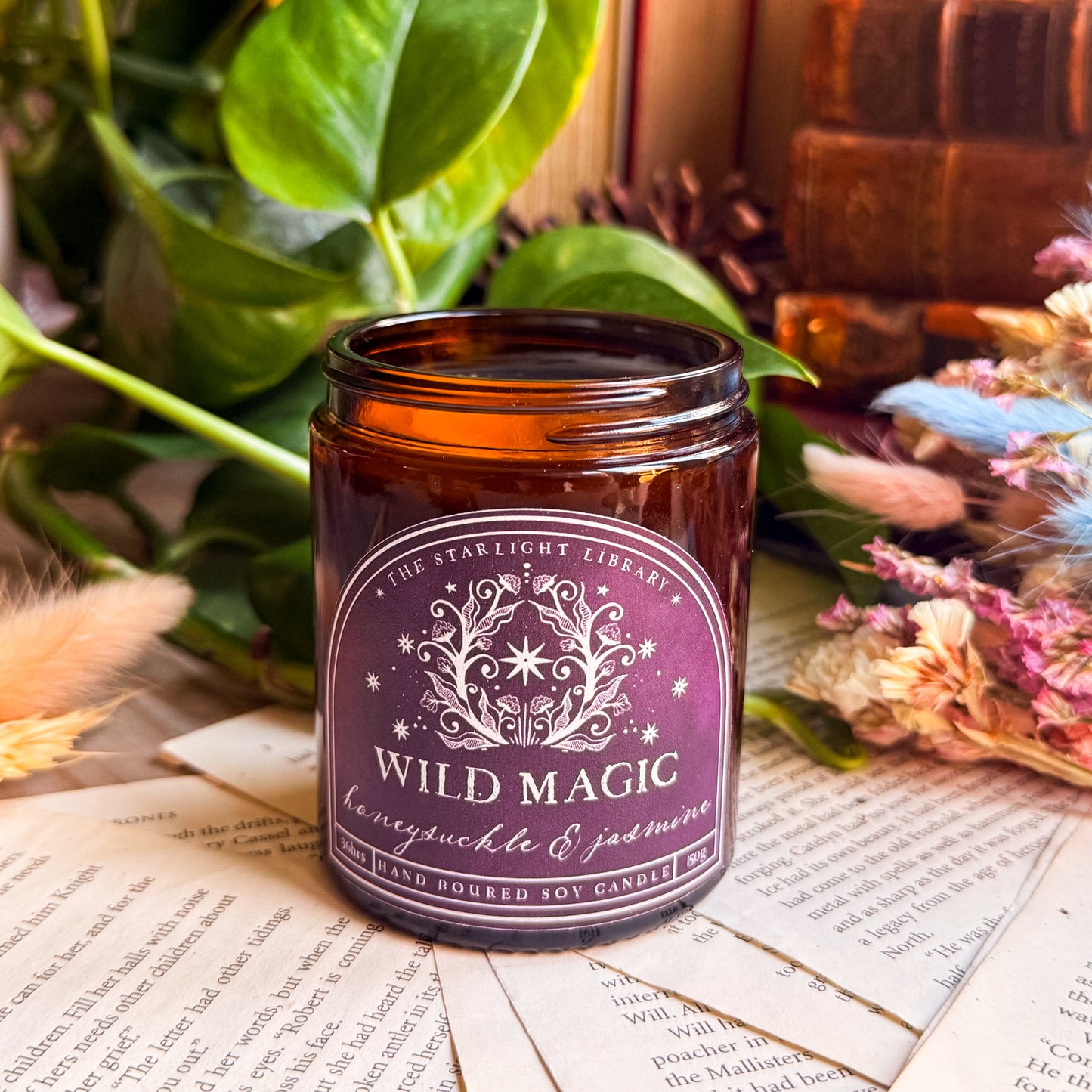 A Wild Magic candle surrounded by book pages, leaves and dried flowers.