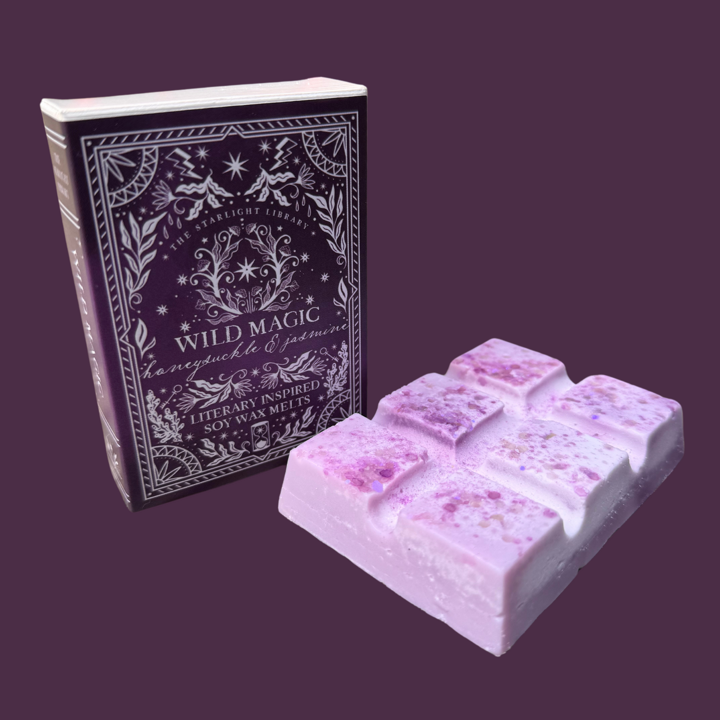 A Wild Magic wax melt , with it's book box, in front of a purple studio background.