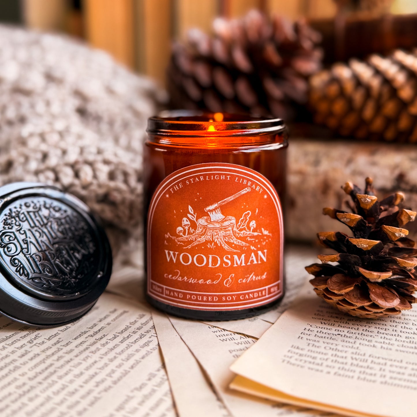 A Woodsman candle, lit, surrounded by old books, pages and pinecones