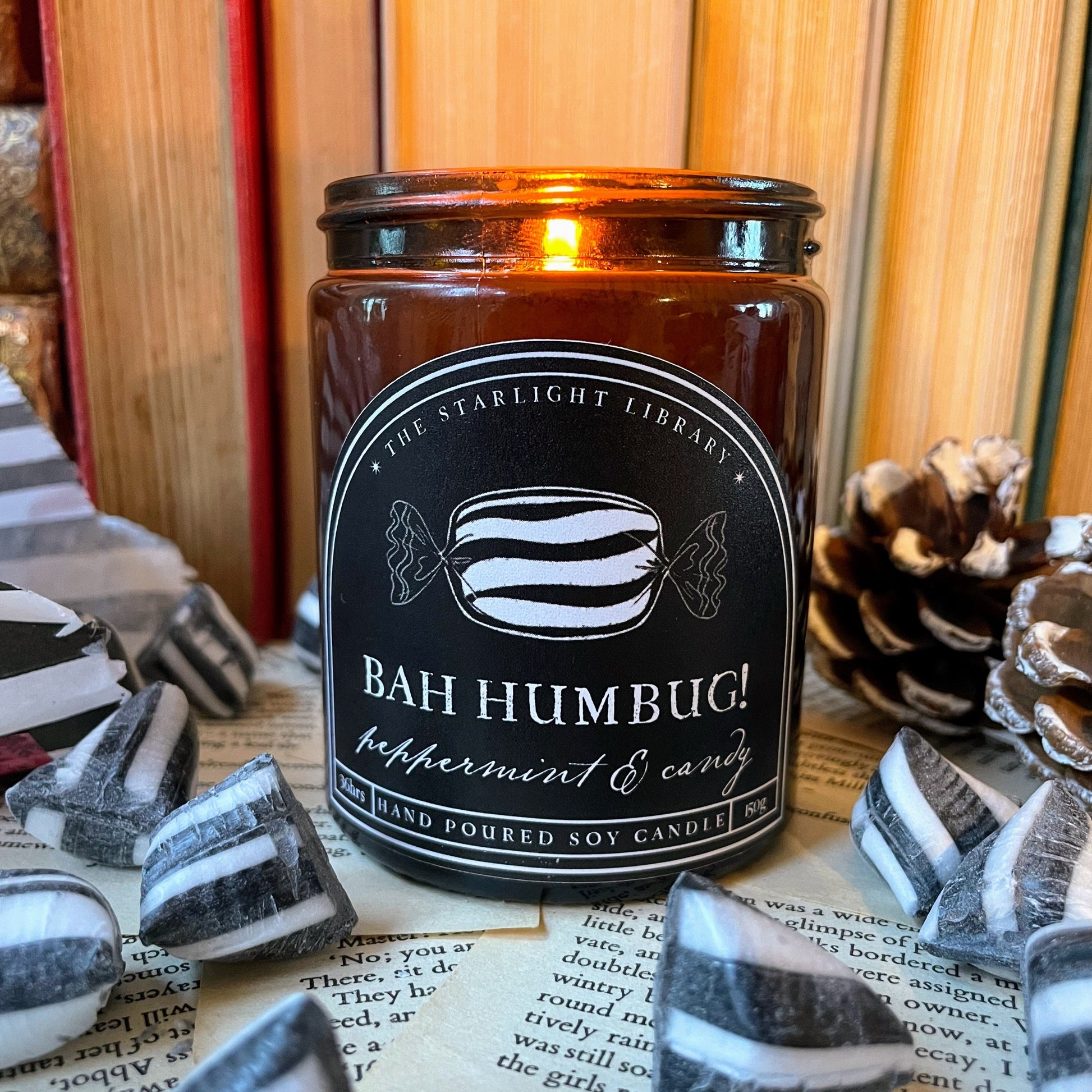 Candle labeled 'Bah Humbug!' on a surface with peppermint candy and books in the background
