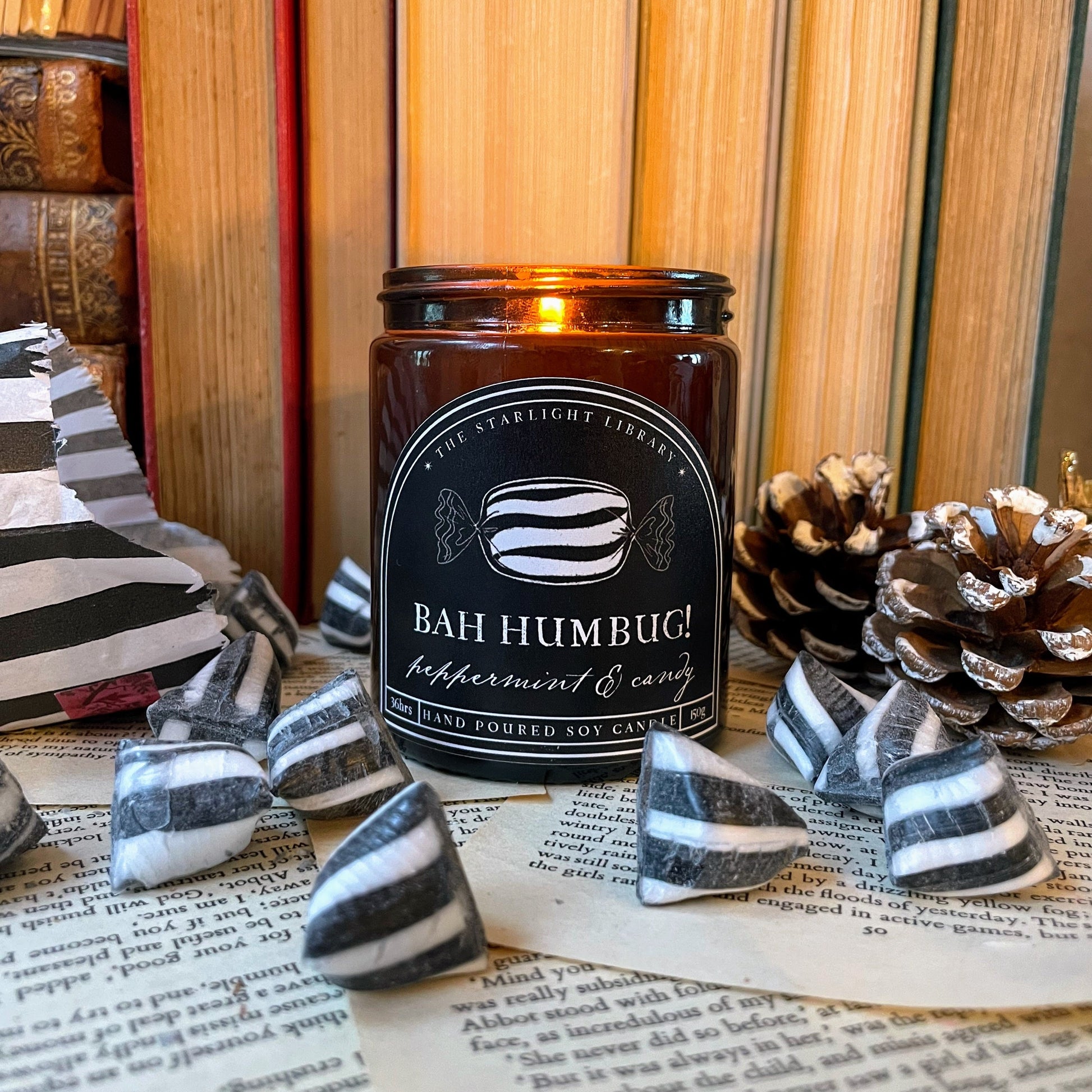 Candle labeled 'Bah Humbug!' with decorative items on a surface with books in the background