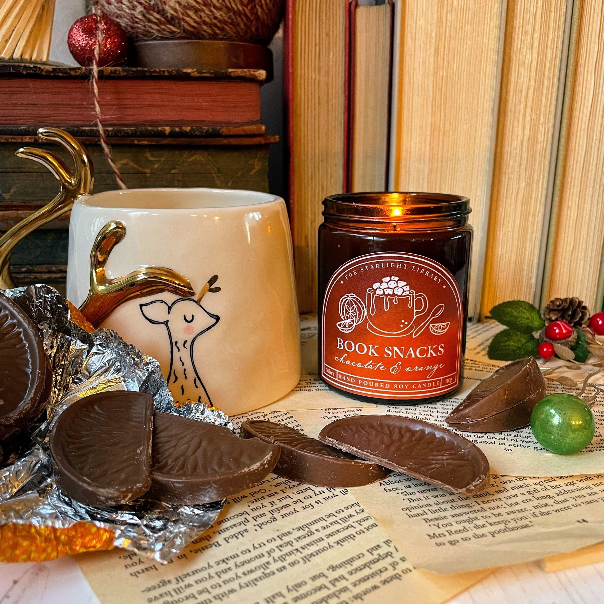 Book-themed snack set with a candle, mug, and chocolate on a surface with books and decorative items.