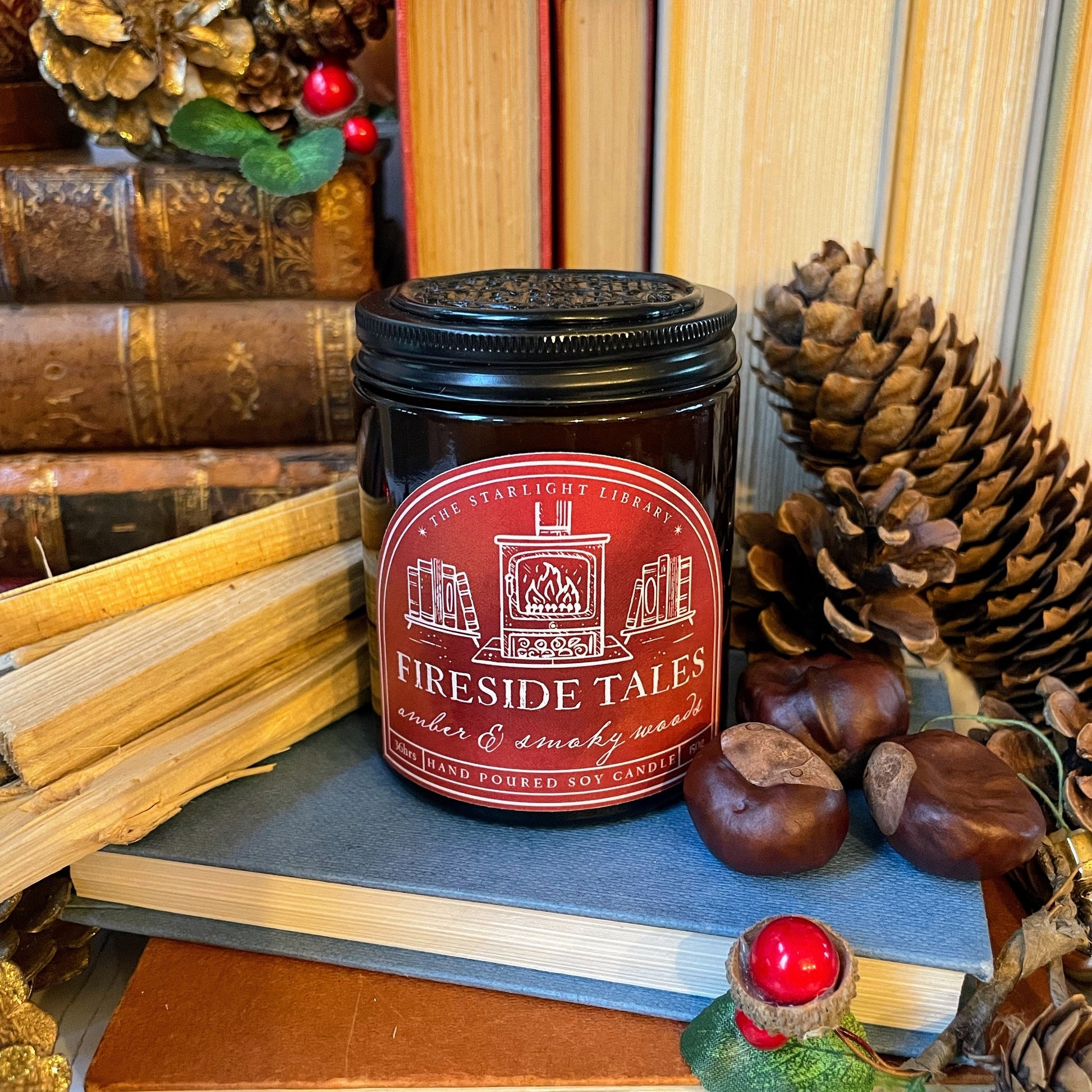 Candle labeled 'Fireside Tales' surrounded by books, pinecones, and chestnuts.