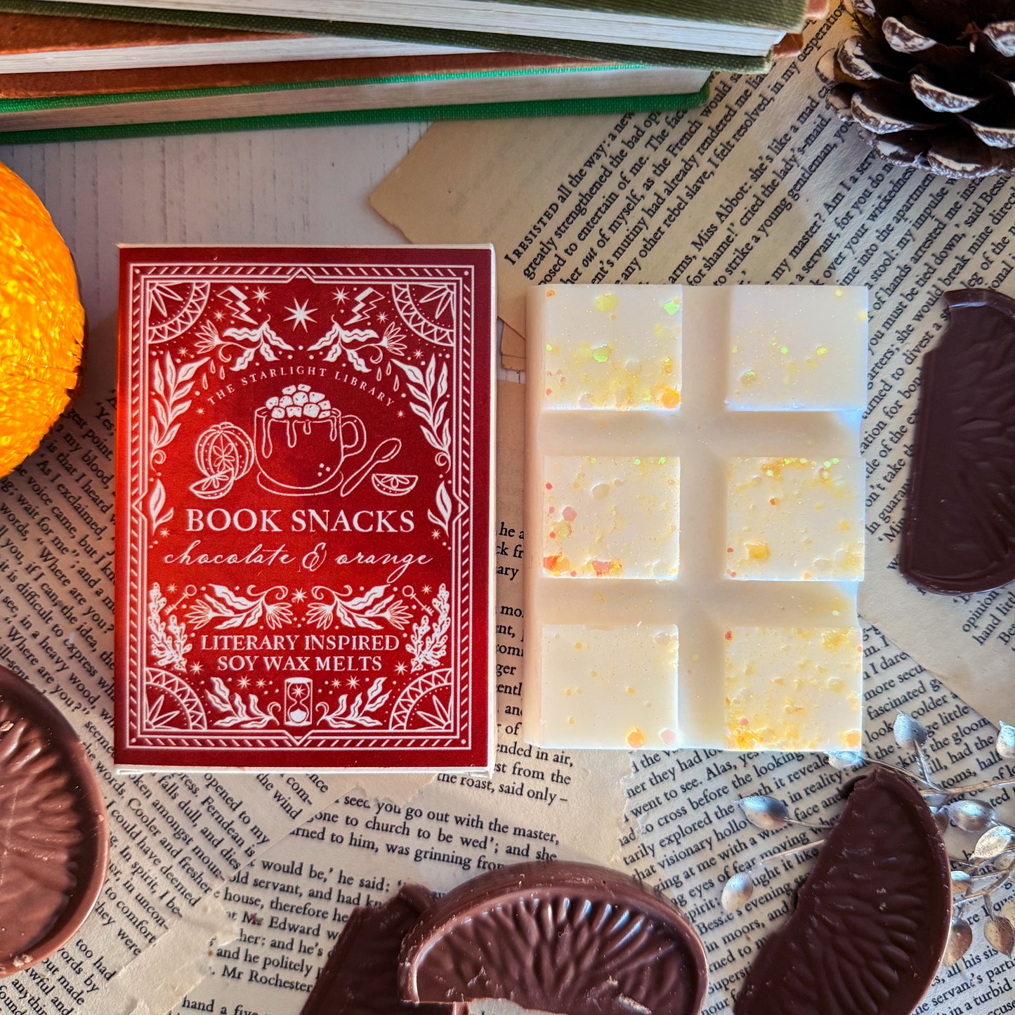 Wax Melts with an orange  box labeled 'Book Snacks' on a surface with text and chocolate pieces.