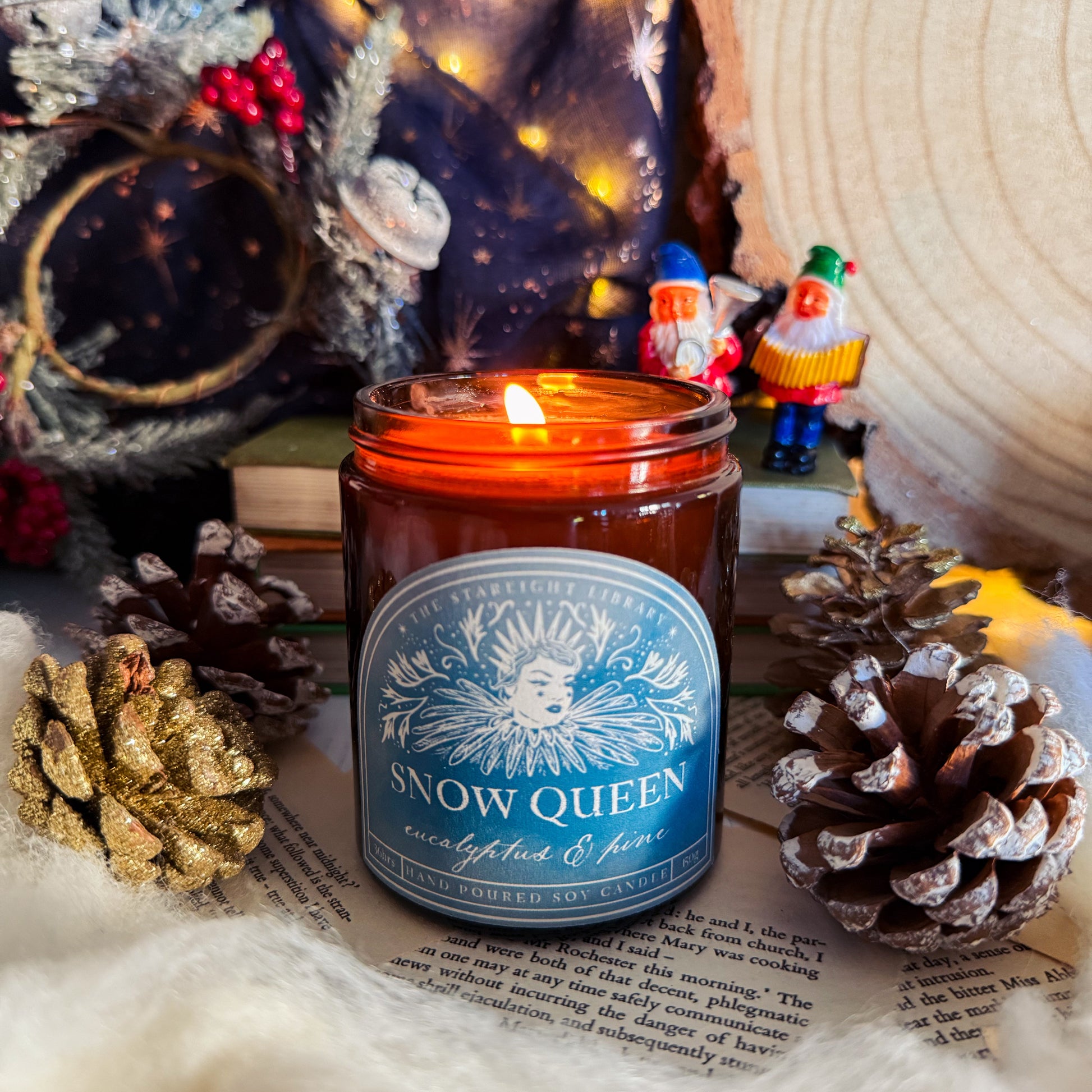 Candle labeled 'Snow Queen' surrounded by decorative items on a textured surface