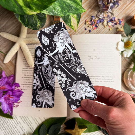 A hand holding the mermaid bookmark above an open book.