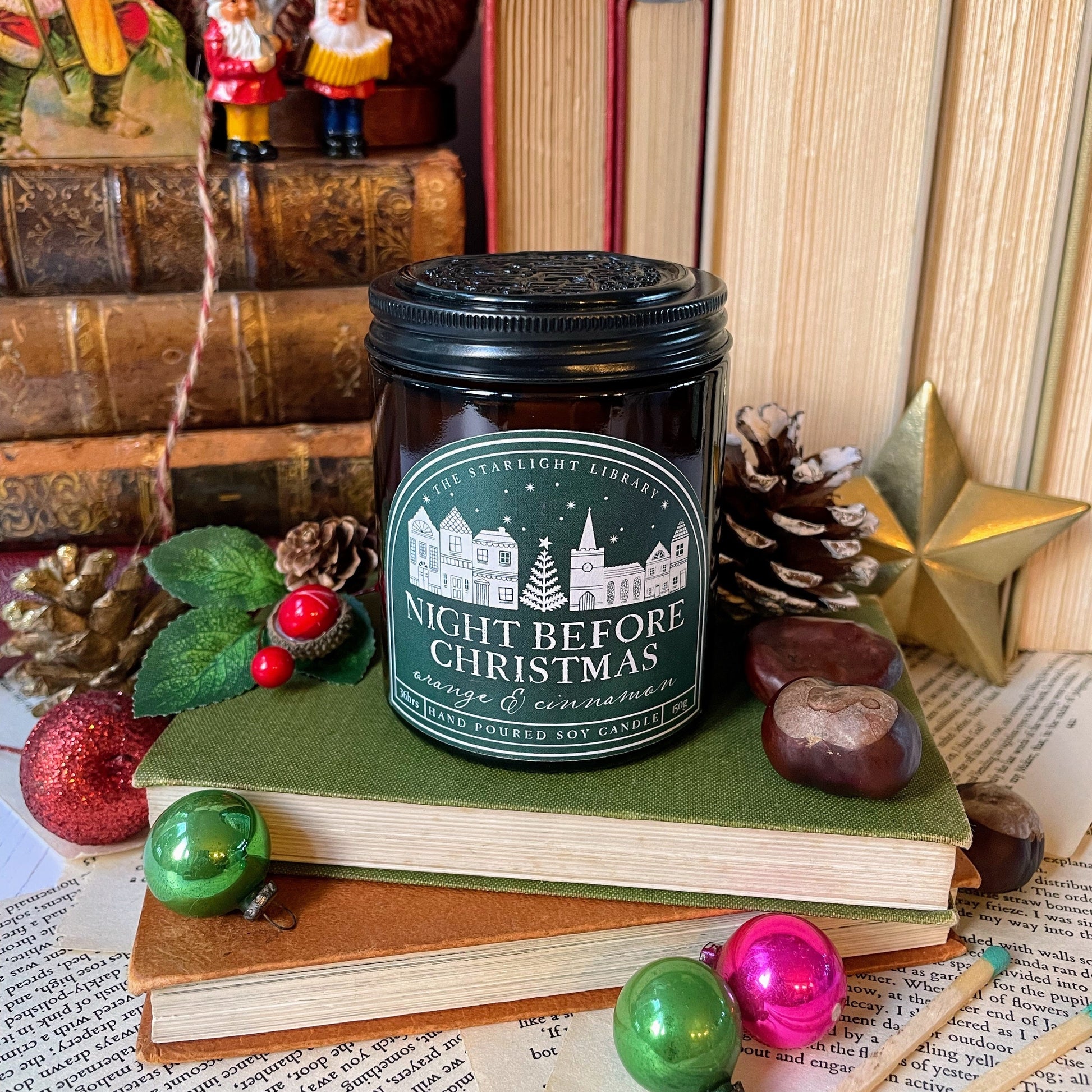 Candle jar labeled 'Night Before Christmas' on books with festive decorations