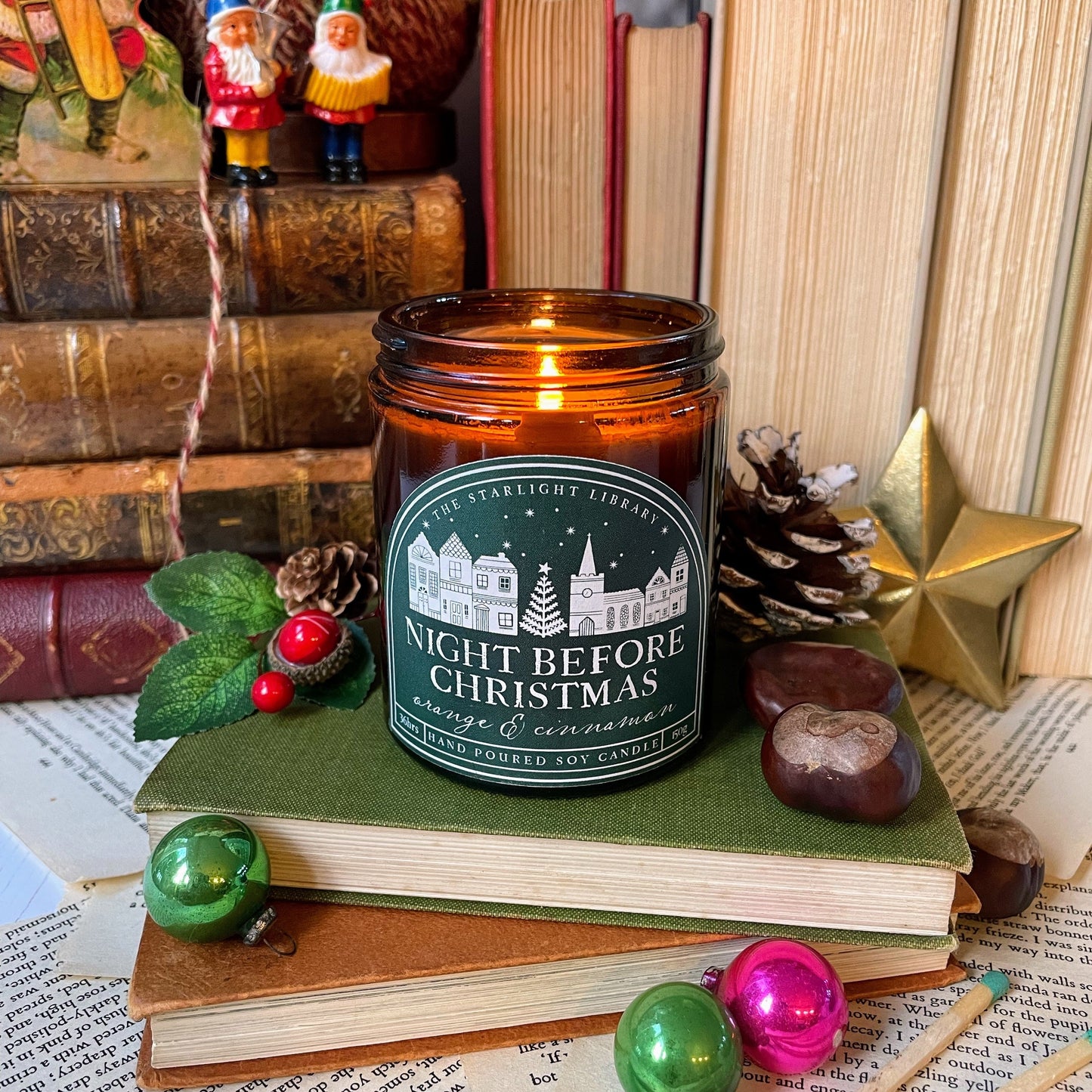 Candle labeled 'Night Before Christmas' on books with festive decorations