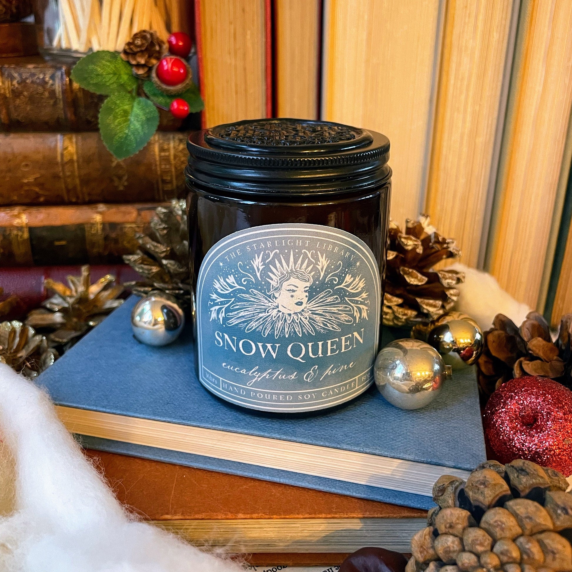 Candle labeled 'Snow Queen' on books with festive decorations