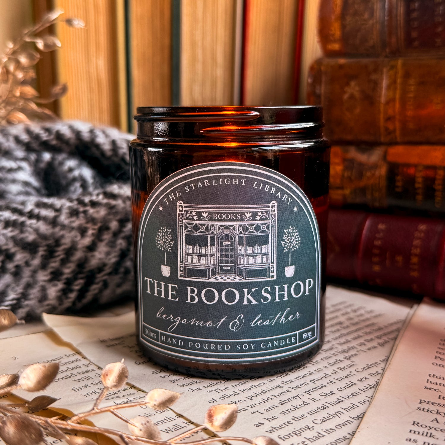 The Bookshop candle, lit, surrounded by old books and pages.