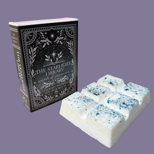 A Starlight Library wax melt bar, with it's book box, in front of a pale purple studio background.