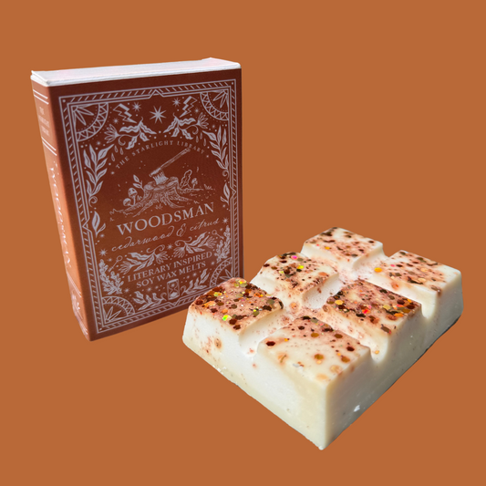 A Woodsman wax melt bar, with it's book box, in front of an orange studio background.